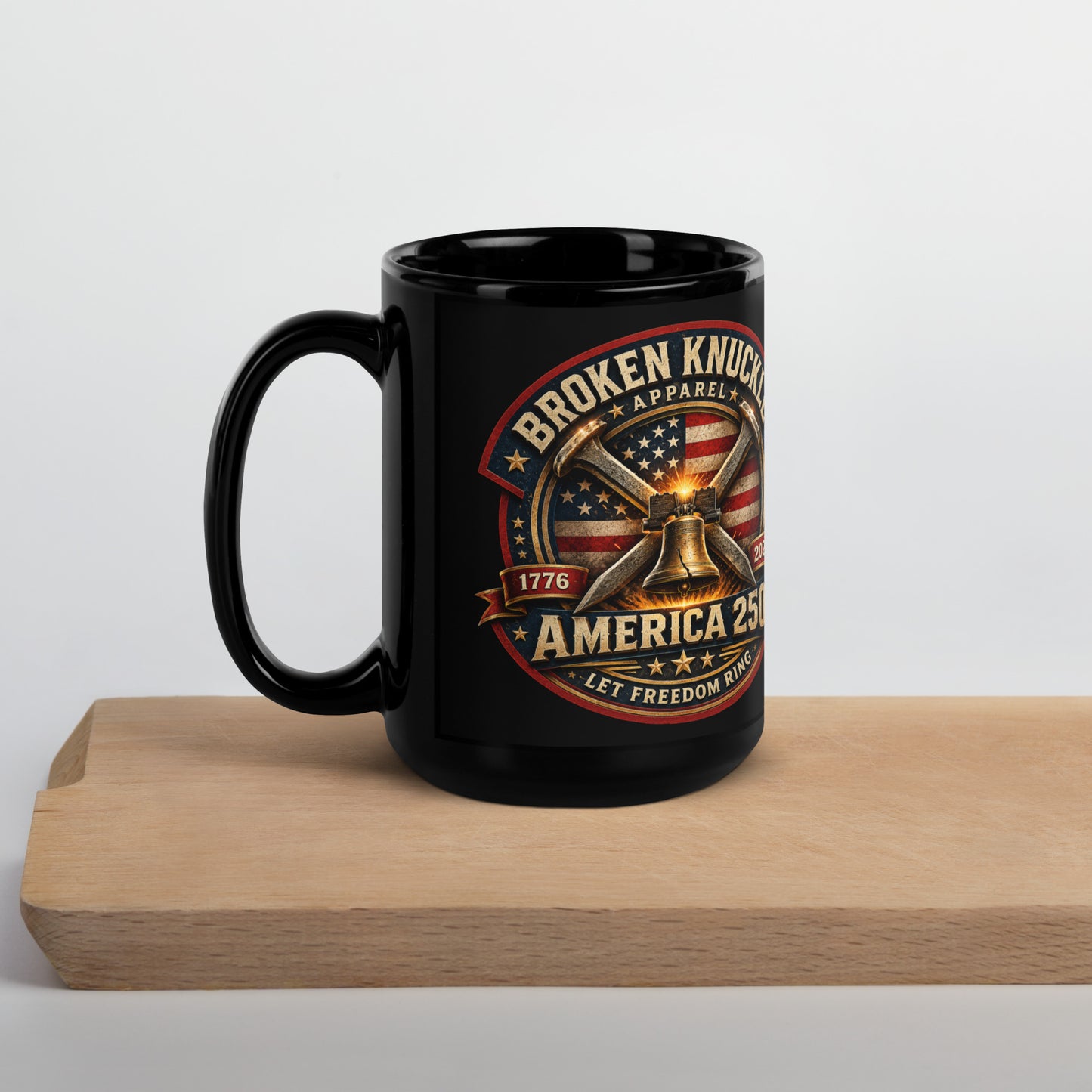 Black 15-ounce glossy coffee mug featuring a circular patriotic graphic. The design includes an American flag background, two crossed railroad spikes, and a glowing Liberty Bell in the center. Text around the badge reads "BROKEN KNUCKLE APPAREL", "1776", "2026", "AMERICA 250", and "LET FREEDOM RING".
