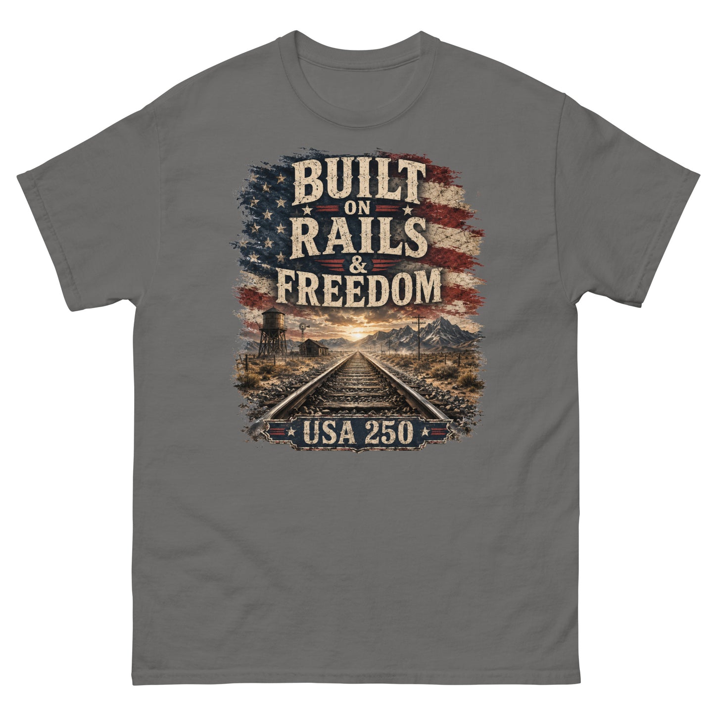 Gray t-shirt featuring a distressed American flag graphic at the top with text reading "BUILT ON RAILS & FREEDOM". Below the text is a landscape illustration of railroad tracks leading toward mountains and a sunset, with a trackside water tower on the left. A banner at the bottom reads "USA 250".