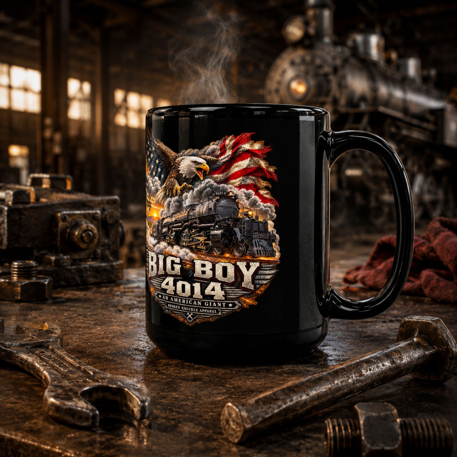 A black ceramic mug with a detailed graphic of a steam locomotive, an American flag, and an eagle, with the text 'BIG BOY 4014' and 'USA AMERICAN GIANT', set on a rustic workbench with tools and a blurred steam engine background.