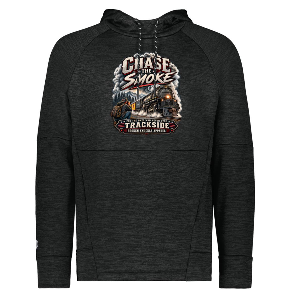 Heather black Holloway performance fleece hoody featuring a graphic of a photographer with a backpack kneeling trackside, taking a picture of a large steam locomotive rolling through a forest landscape. Bold distressed text reads "CHASE THE SMOKE" at the top and "FOR THE ONES WHO NEVER STOP TRACKSIDE" in a vintage banner at the bottom.