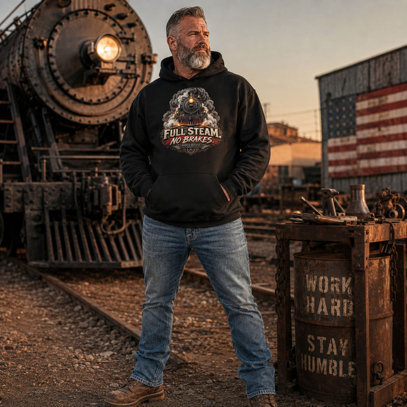 A bearded man wearing a black hoodie with a 'Full Steam No Brakes' dog graphic stands on railroad tracks in an industrial yard with a vintage train, a wooden barrel, and an American flag in the background.