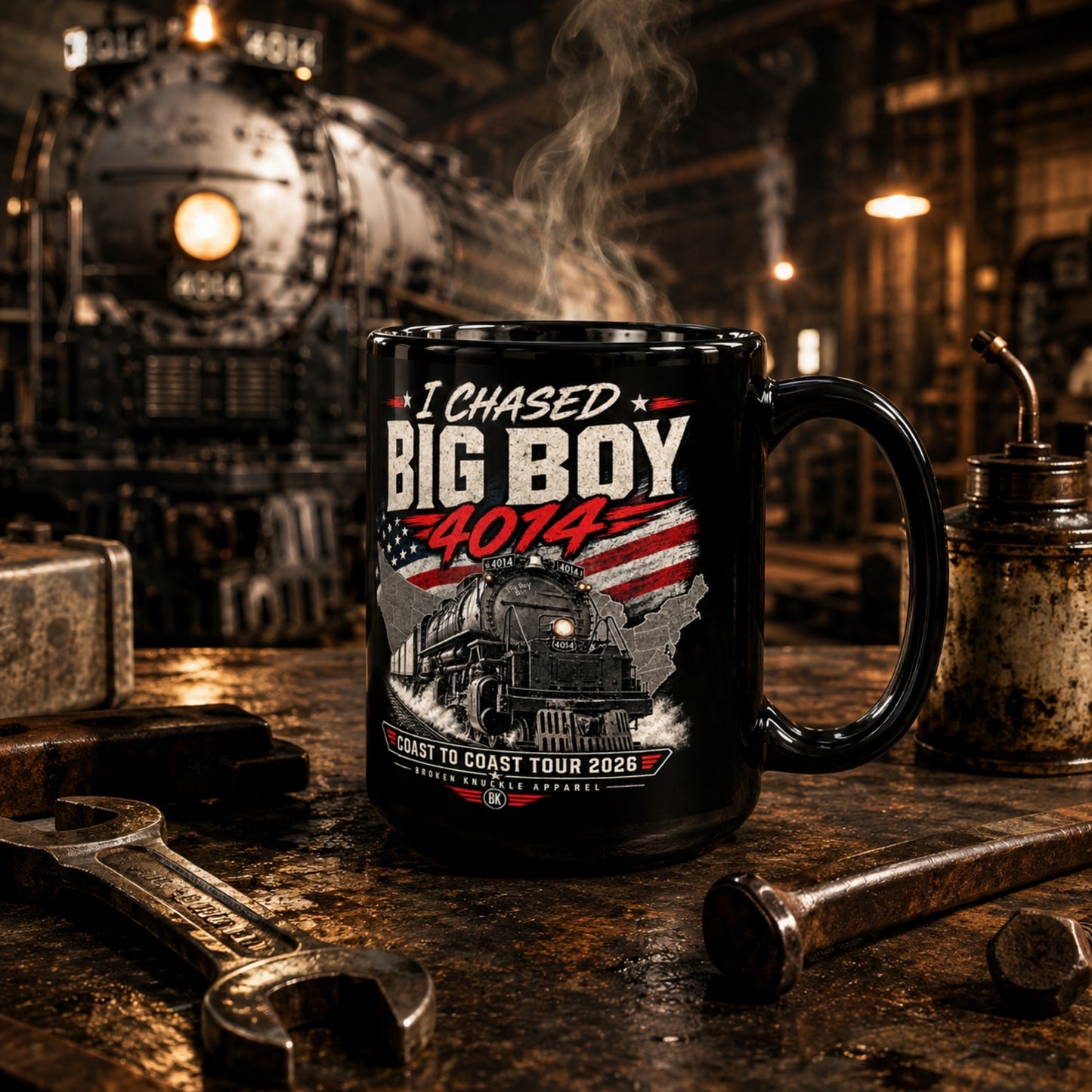 A black ceramic mug with a detailed graphic print of a steam locomotive and the text 'I Chased BIG BOY 4014' and 'COAST TO COAST TOUR 2026', set on a rustic workbench with wrenches and a blurred train engine in the background.