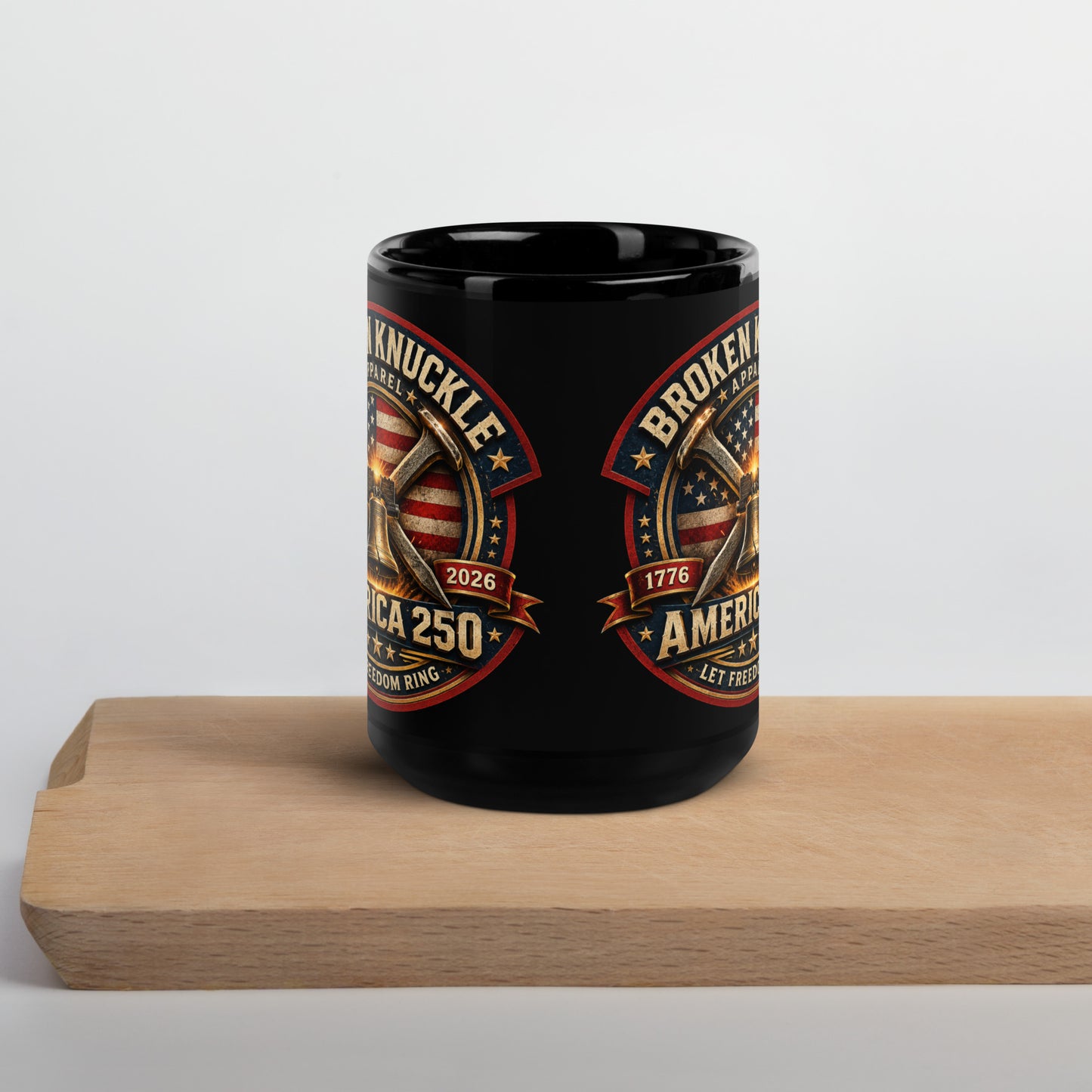 Black 15-ounce glossy coffee mug featuring a circular patriotic graphic. The design includes an American flag background, two crossed railroad spikes, and a glowing Liberty Bell in the center. Text around the badge reads "BROKEN KNUCKLE APPAREL", "1776", "2026", "AMERICA 250", and "LET FREEDOM RING".