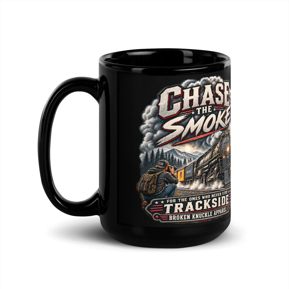 Black glossy 15 oz ceramic mug featuring a graphic of a photographer with a backpack kneeling trackside, taking a picture of a large steam locomotive. Bold distressed text reads "CHASE THE SMOKE" at the top and "FOR THE ONES WHO NEVER STOP TRACKSIDE" in a vintage banner at the bottom.