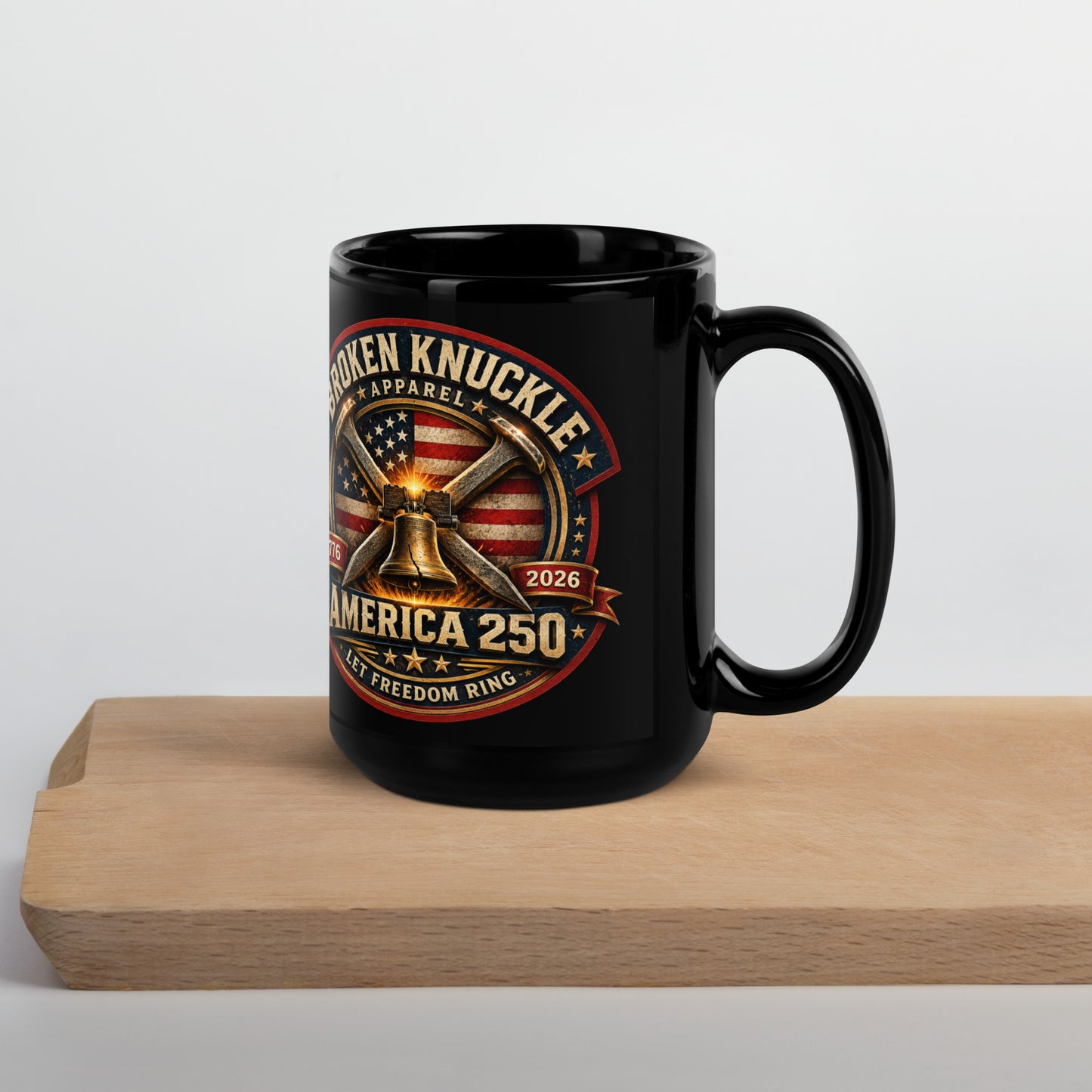 Black 15-ounce glossy coffee mug featuring a circular patriotic graphic. The design includes an American flag background, two crossed railroad spikes, and a glowing Liberty Bell in the center. Text around the badge reads "BROKEN KNUCKLE APPAREL", "1776", "2026", "AMERICA 250", and "LET FREEDOM RING".