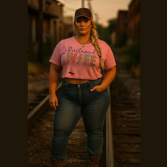Woman wearing a pink t-shirt with text and jeans standing on train tracks.