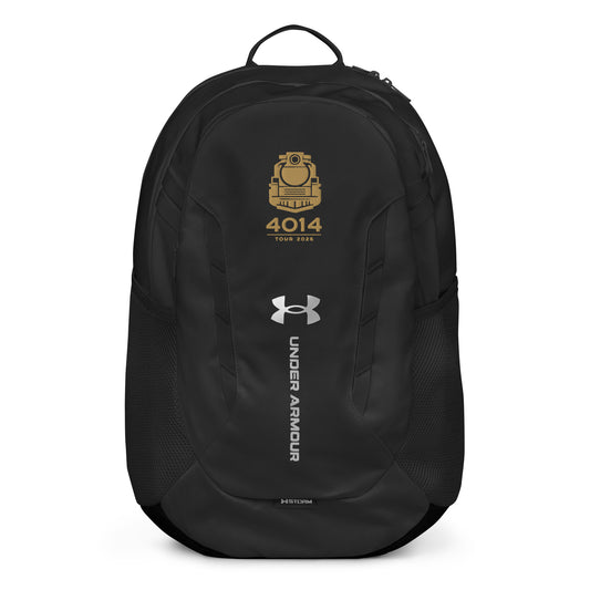 Black Under Armour backpack featuring a gold graphic of a front-facing steam locomotive above the text "4014 TOUR 2026". The silver Under Armour logo is centered on the front above the vertical text "UNDER ARMOUR". The bottom of the bag features the UA Storm technology badge.