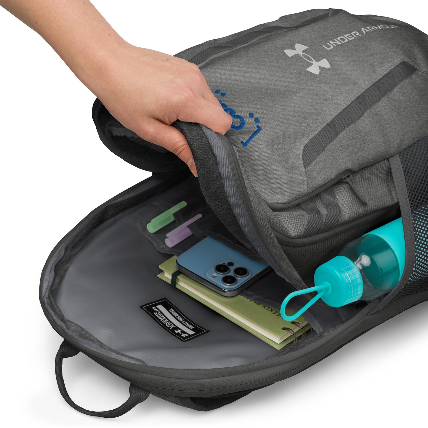 Gray Under Armour backpack with items like a phone and water bottle inside, on a white background