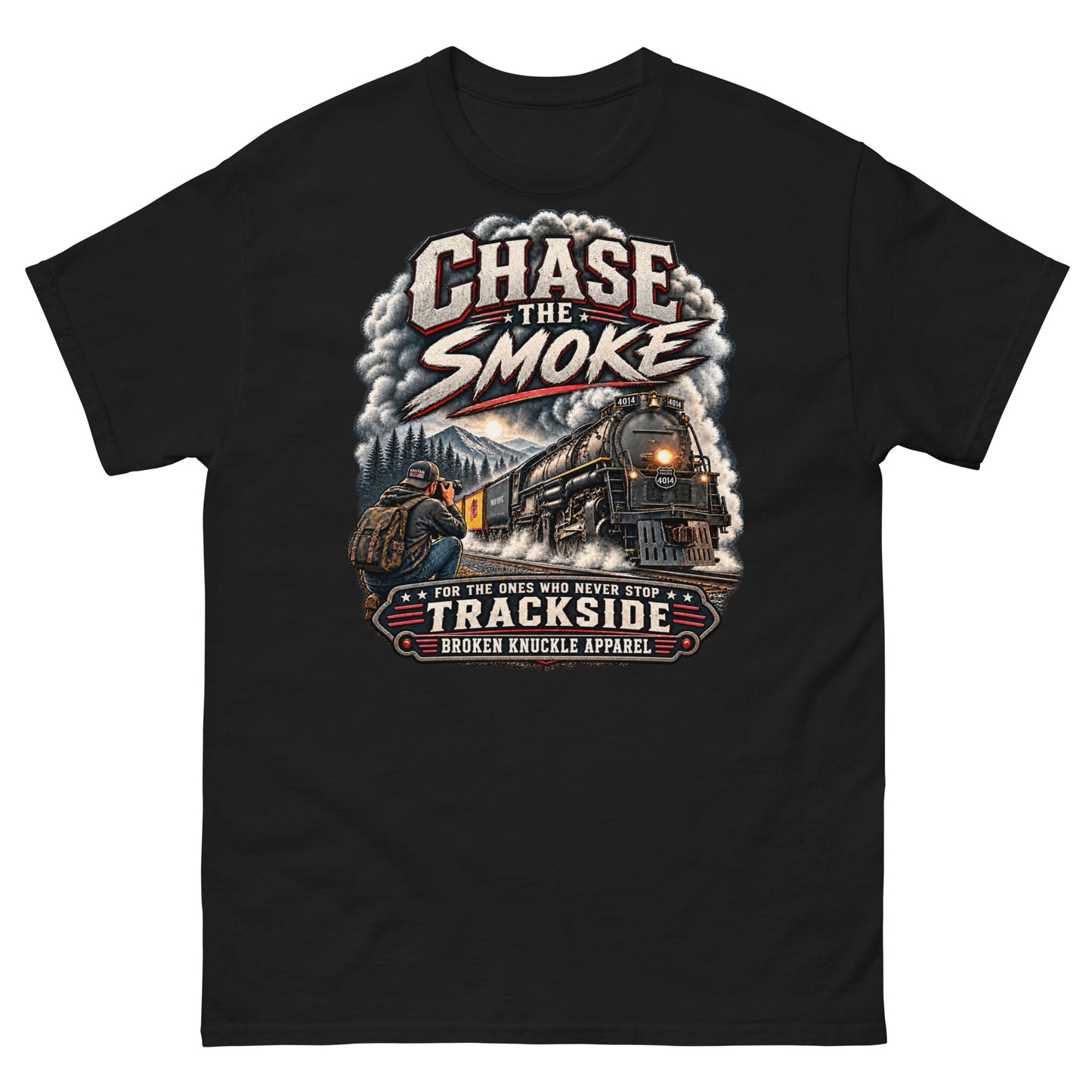 Black classic t-shirt featuring a graphic of a photographer with a backpack kneeling trackside, taking a picture of a large steam locomotive rolling through a forest landscape under a setting sun. Massive plumes of smoke billow into the sky. Bold distressed text at the top reads "CHASE THE SMOKE". A vintage banner at the bottom reads "FOR THE ONES WHO NEVER STOP", "TRACKSIDE", and "BROKEN KNUCKLE APPAREL".
