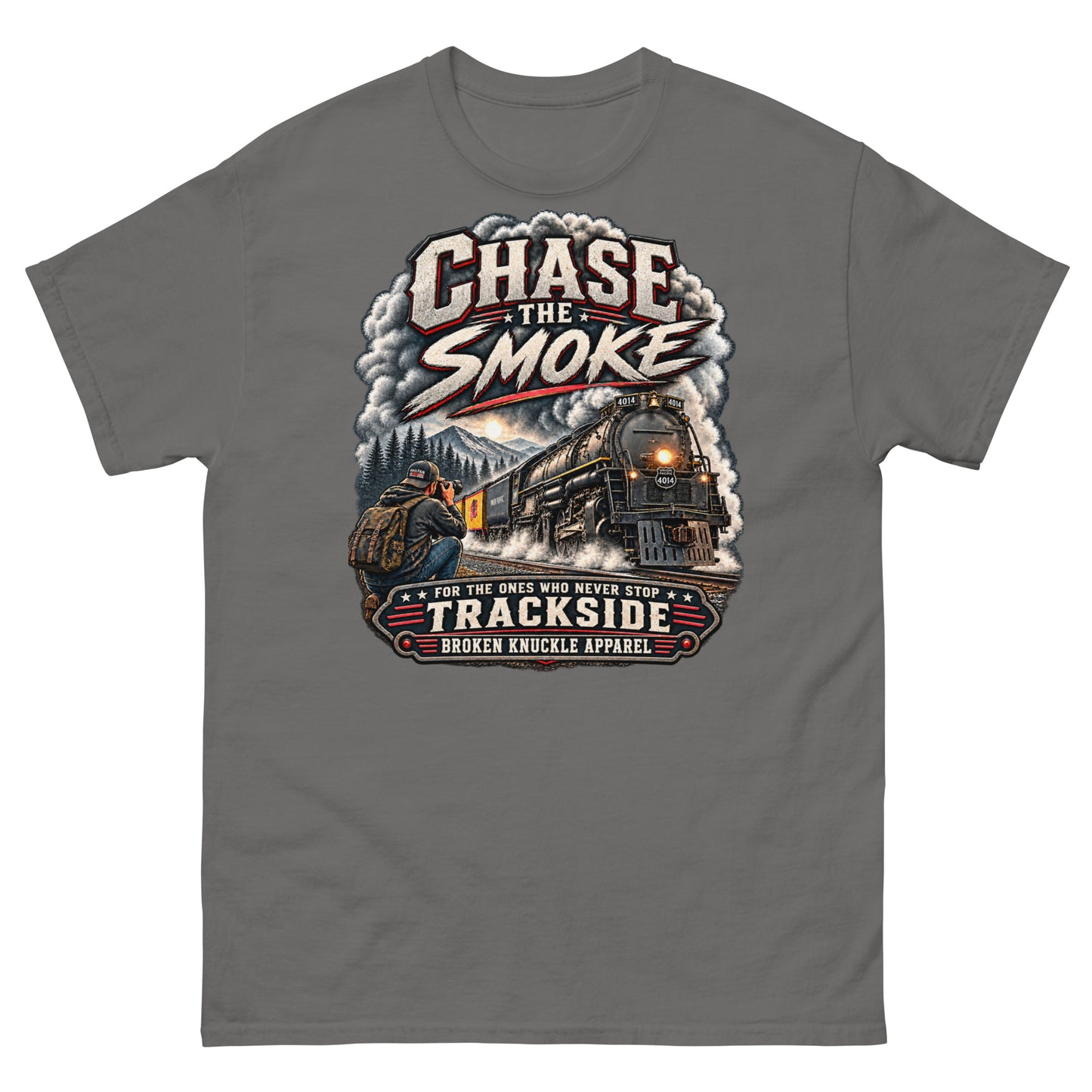 Charcoal classic t-shirt featuring a graphic of a photographer with a backpack kneeling trackside, taking a picture of a large steam locomotive rolling through a forest landscape under a setting sun. Massive plumes of smoke billow into the sky. Bold distressed text at the top reads "CHASE THE SMOKE". A vintage banner at the bottom reads "FOR THE ONES WHO NEVER STOP", "TRACKSIDE", and "BROKEN KNUCKLE APPAREL".