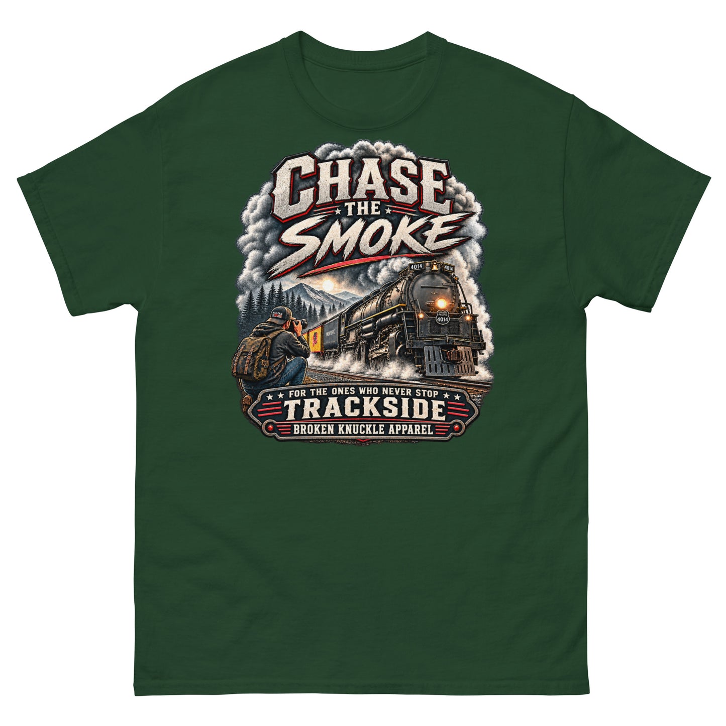 Forest green classic t-shirt featuring a graphic of a photographer with a backpack kneeling trackside, taking a picture of a large steam locomotive rolling through a forest landscape under a setting sun. Massive plumes of smoke billow into the sky. Bold distressed text at the top reads "CHASE THE SMOKE". A vintage banner at the bottom reads "FOR THE ONES WHO NEVER STOP", "TRACKSIDE", and "BROKEN KNUCKLE APPAREL".
