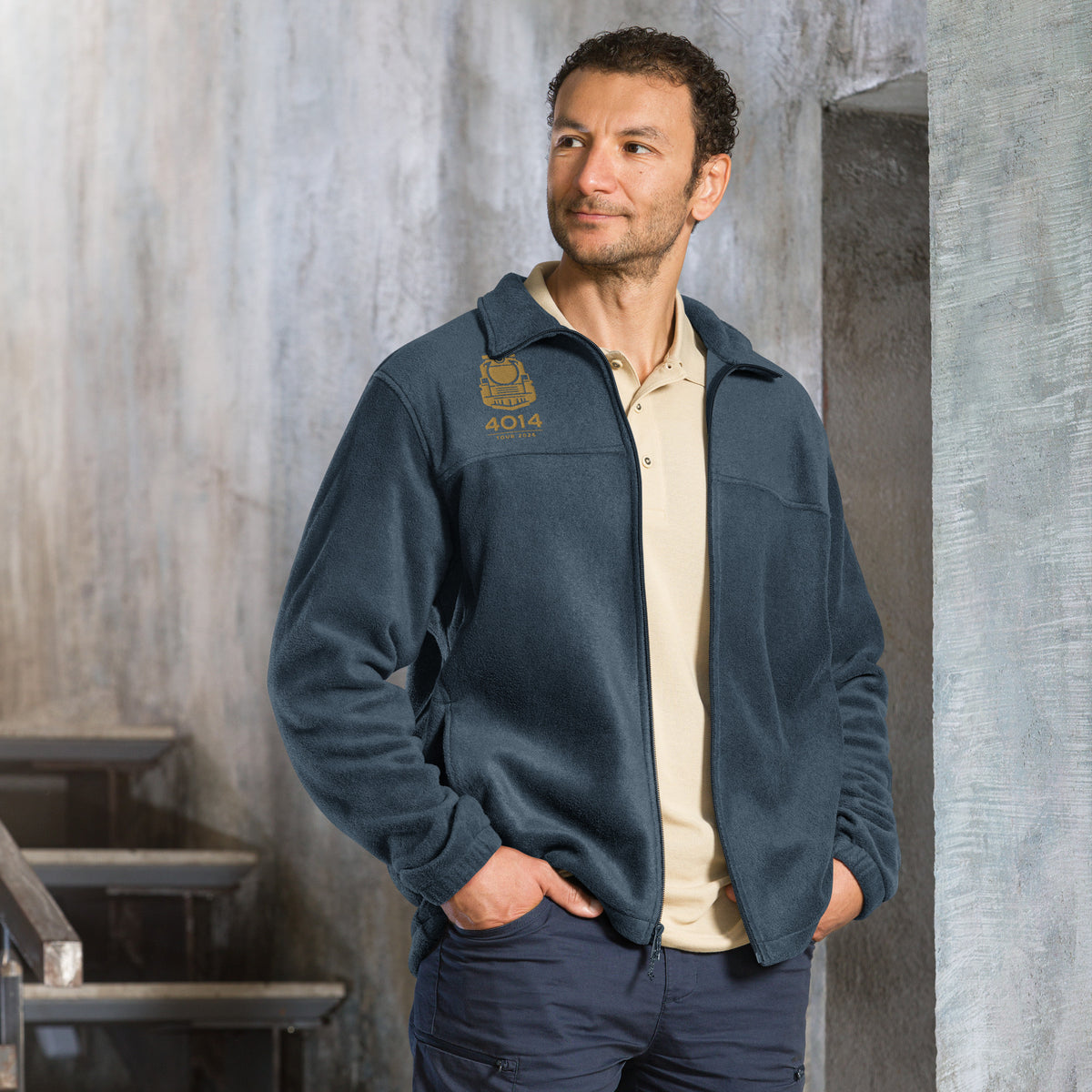 Man wearing a dark blue Columbia full-zip fleece jacket featuring a gold embroidered graphic of a front-facing steam locomotive above the text "4014 TOUR 2026" on the right chest. A white Columbia logo is visible on the left sleeve.