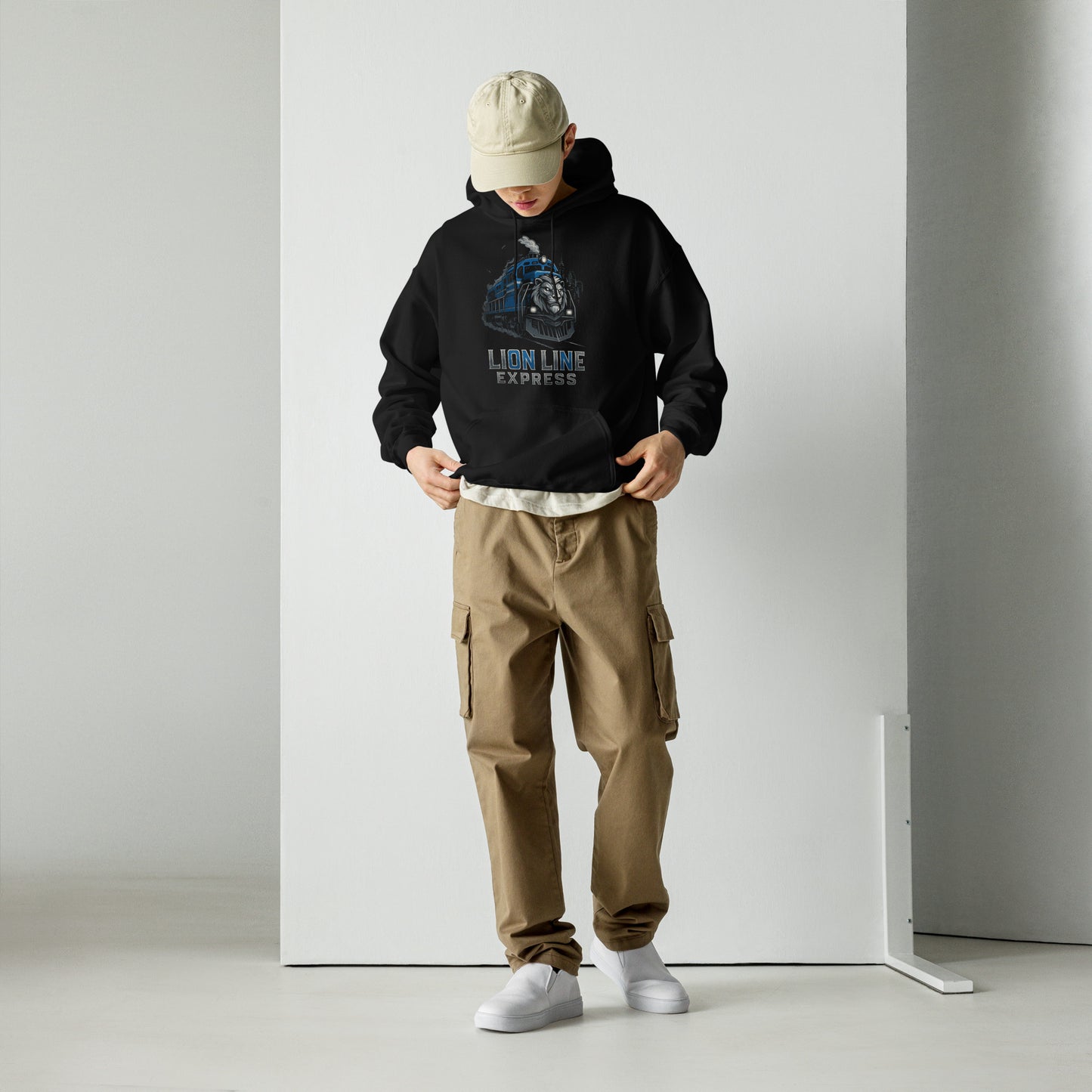 Person wearing a black hoodie with a graphic design, beige cap, and brown cargo pants against a white background.
