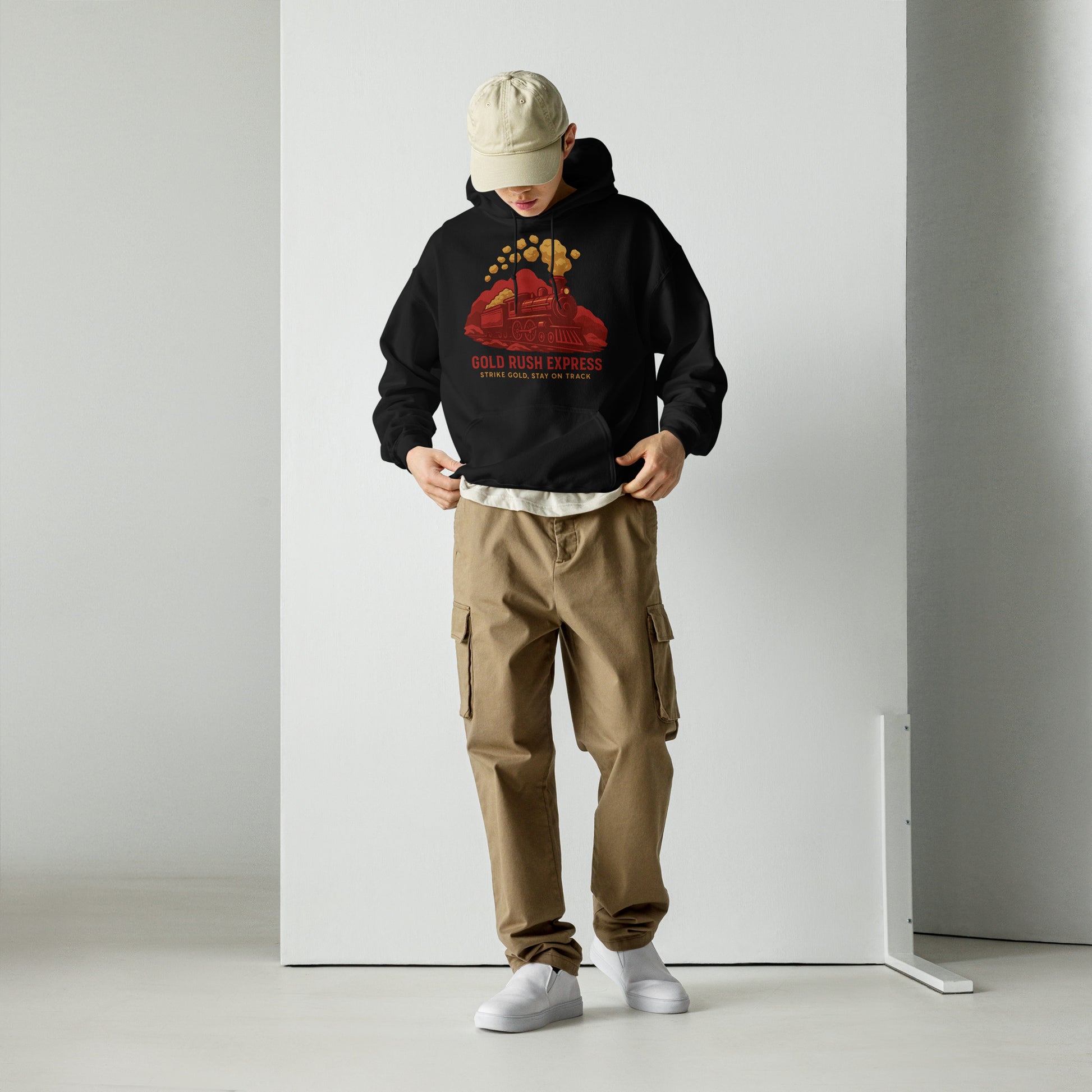 Person wearing a black hoodie with a red graphic and text, beige cap, brown cargo pants, and white shoes on a plain background.