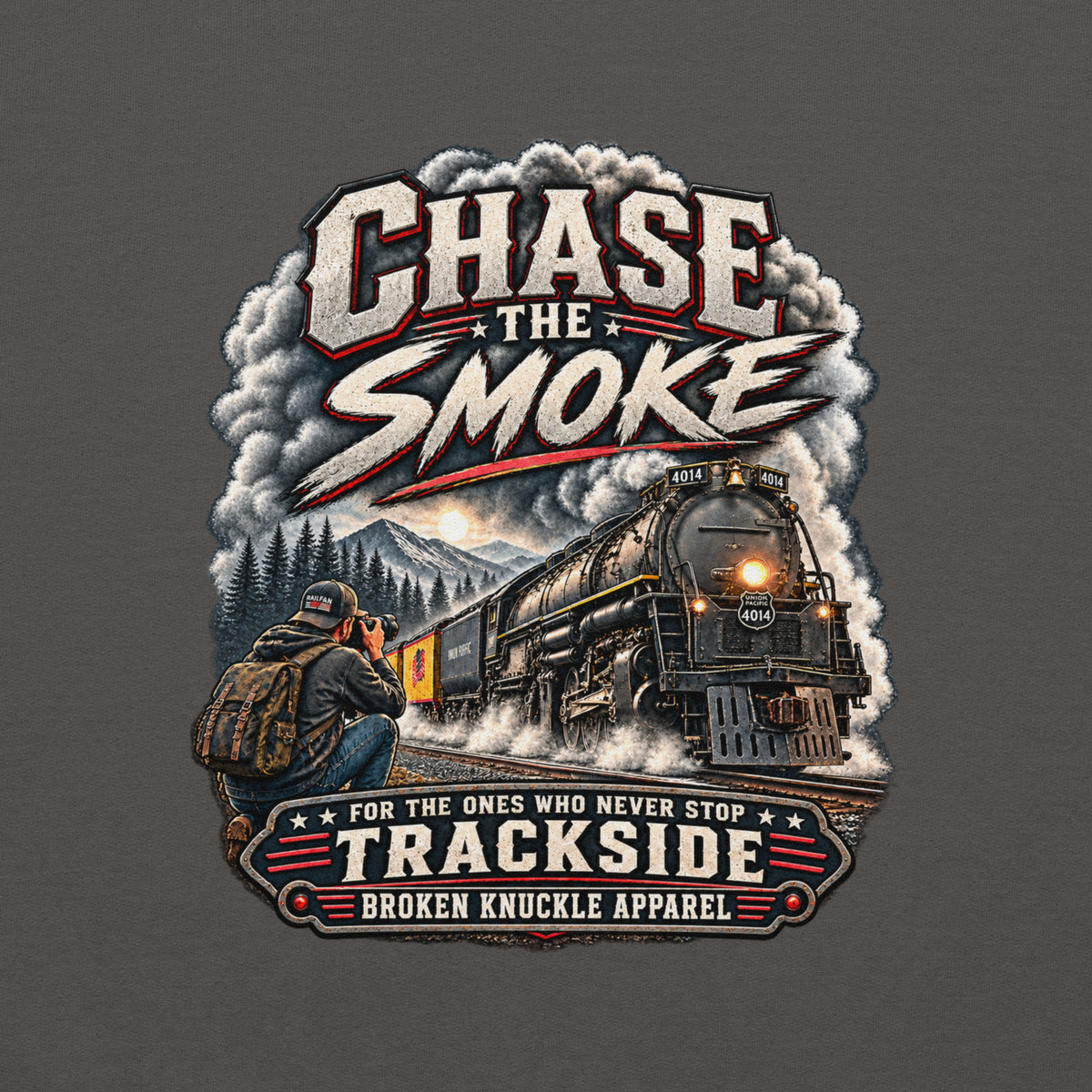 Charcoal heavy blend pullover hoodie featuring a graphic of a photographer with a backpack kneeling trackside, taking a picture of a large steam locomotive rolling through a forest landscape. Bold distressed text reads "CHASE THE SMOKE" at the top and "FOR THE ONES WHO NEVER STOP TRACKSIDE" in a vintage banner at the bottom.
