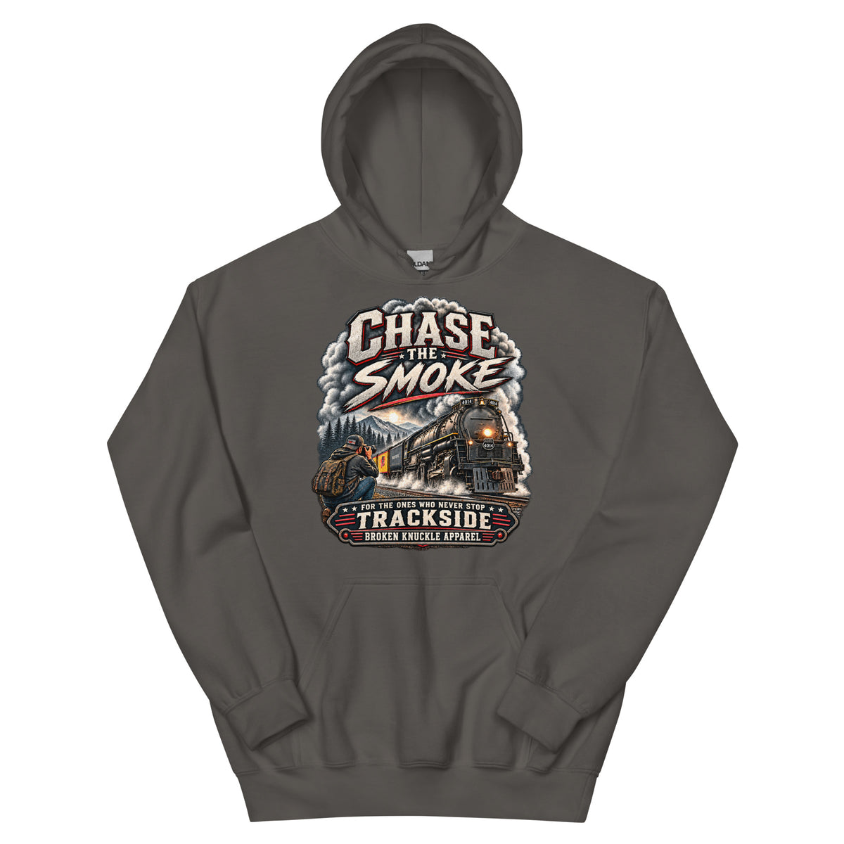 Charcoal heavy blend pullover hoodie featuring a graphic of a photographer with a backpack kneeling trackside, taking a picture of a large steam locomotive rolling through a forest landscape. Bold distressed text reads "CHASE THE SMOKE" at the top and "FOR THE ONES WHO NEVER STOP TRACKSIDE" in a vintage banner at the bottom.