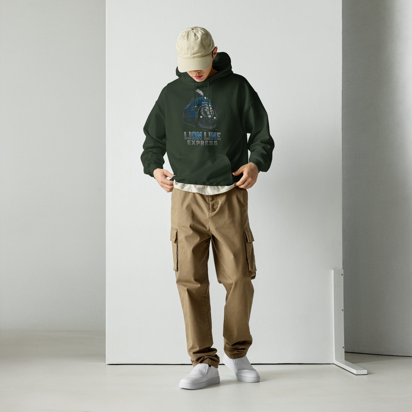 Person wearing a dark green hoodie and brown cargo pants standing against a white wall.