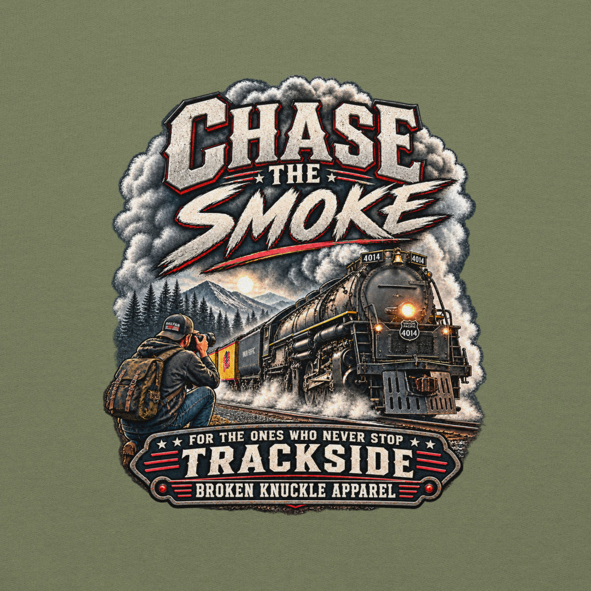 Army green heavy blend pullover hoodie featuring a graphic of a photographer with a backpack kneeling trackside, taking a picture of a large steam locomotive rolling through a forest landscape. Bold distressed text reads "CHASE THE SMOKE" at the top and "FOR THE ONES WHO NEVER STOP TRACKSIDE" in a vintage banner at the bottom.
