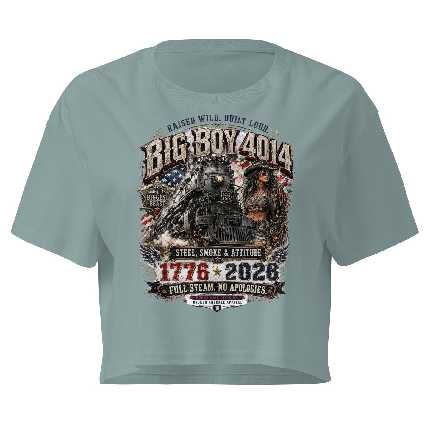Green women's crop top featuring a gritty graphic of the Big Boy 4014 steam locomotive next to a woman in a cowboy hat and leather jacket. The background includes a distressed American flag and eagle wings. Text reads "RAISED WILD. BUILT LOUD.", "BIG BOY 4014", "AMERICA'S BIGGEST BEAST", "STEEL, SMOKE & ATTITUDE", "1776 - 2026", "FULL STEAM. NO APOLOGIES.", and "RODEO RAIL DIVISION".