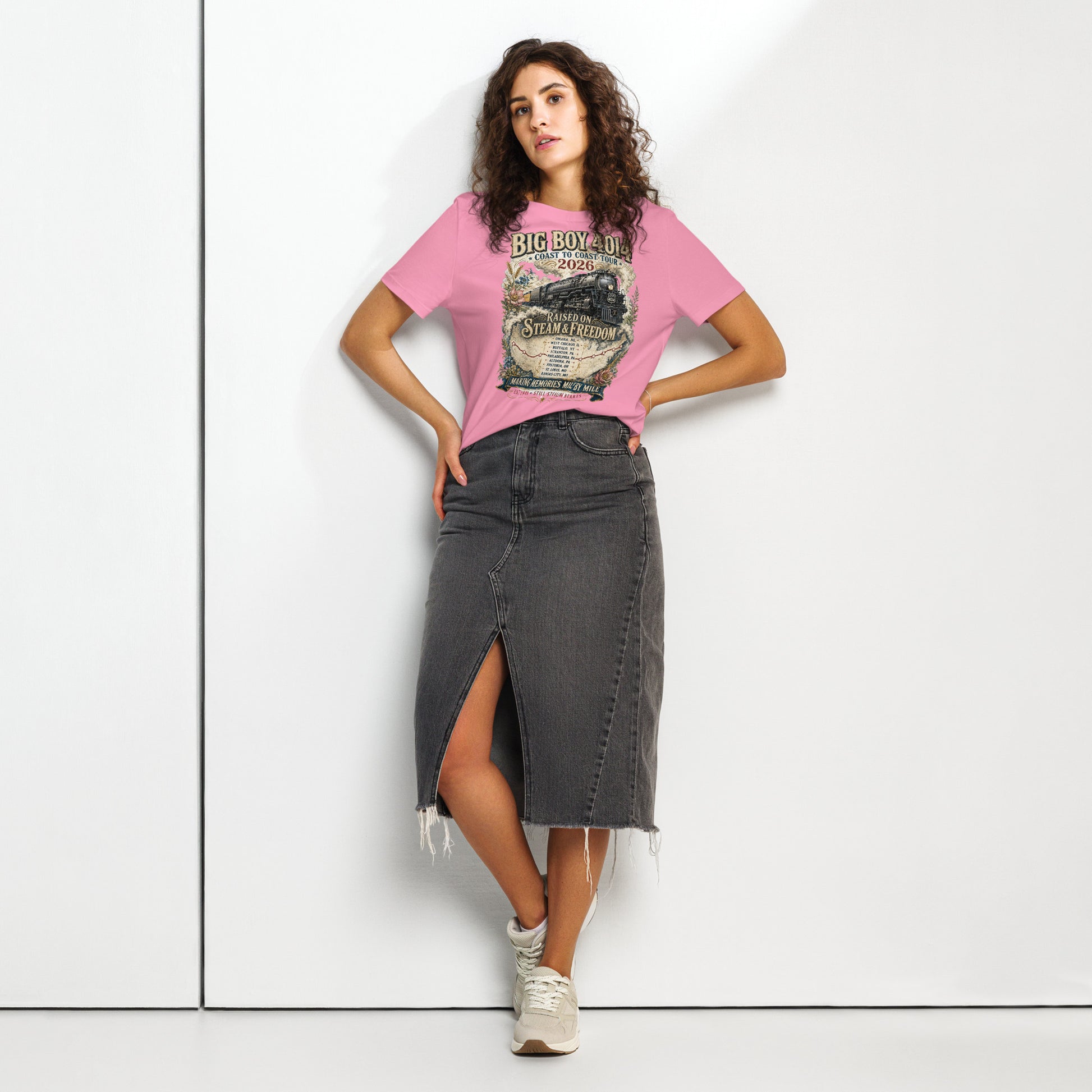 Woman wearing a pink t-shirt featuring a vintage illustration of the Big Boy 4014 steam locomotive surrounded by floral accents, a tour map, and text reading "BIG BOY 4014", "COAST TO COAST TOUR 2026", "RAISED ON STEAM & FREEDOM", and "MAKING MEMORIES MILE BY MILE".