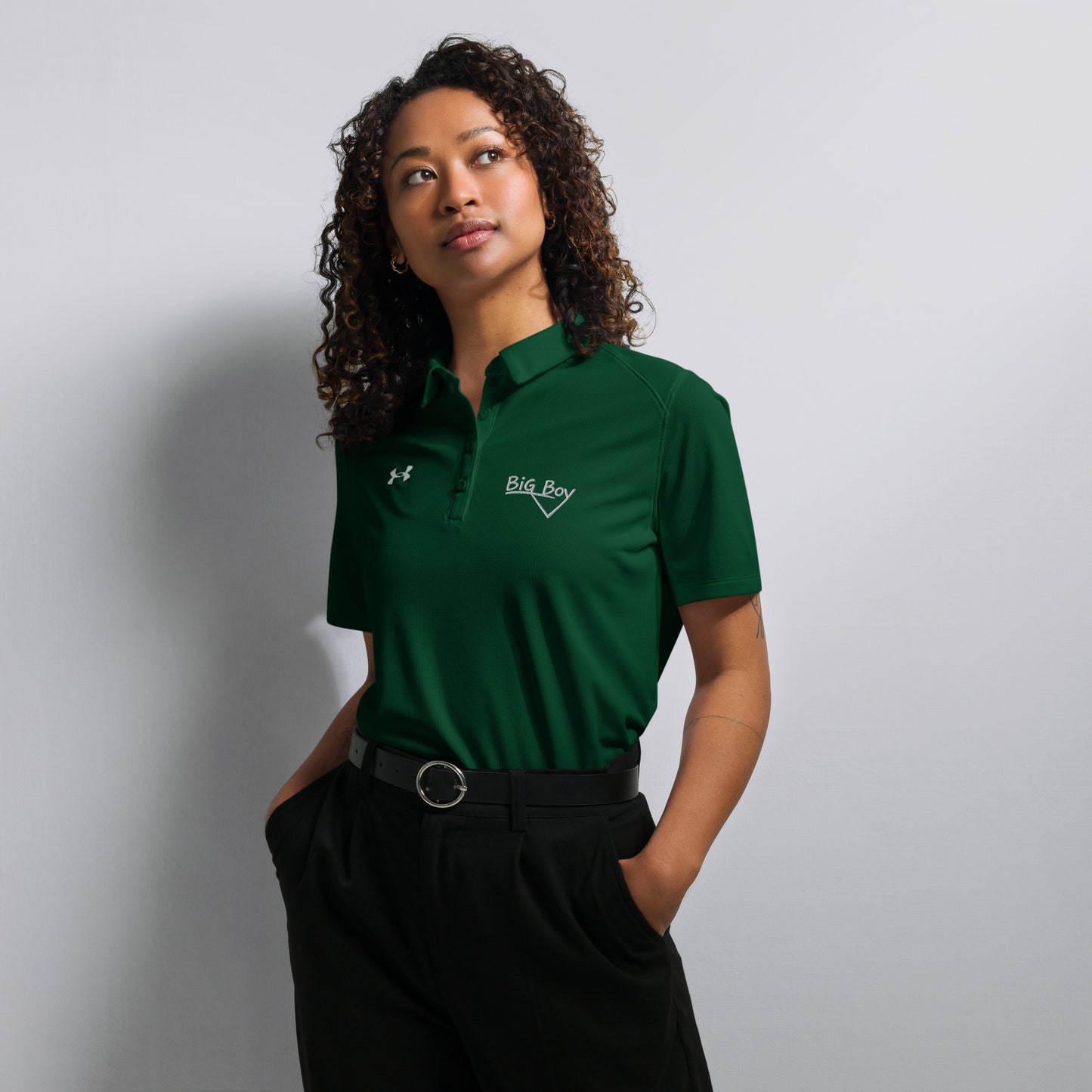 Forest green Under Armour women's polo shirt featuring the classic white chalk-style "Big Boy" script logo on the left chest. A white Under Armour logo is displayed on the right chest. The shirt has a classic collar and a multi-button placket tailored for a women's fit.