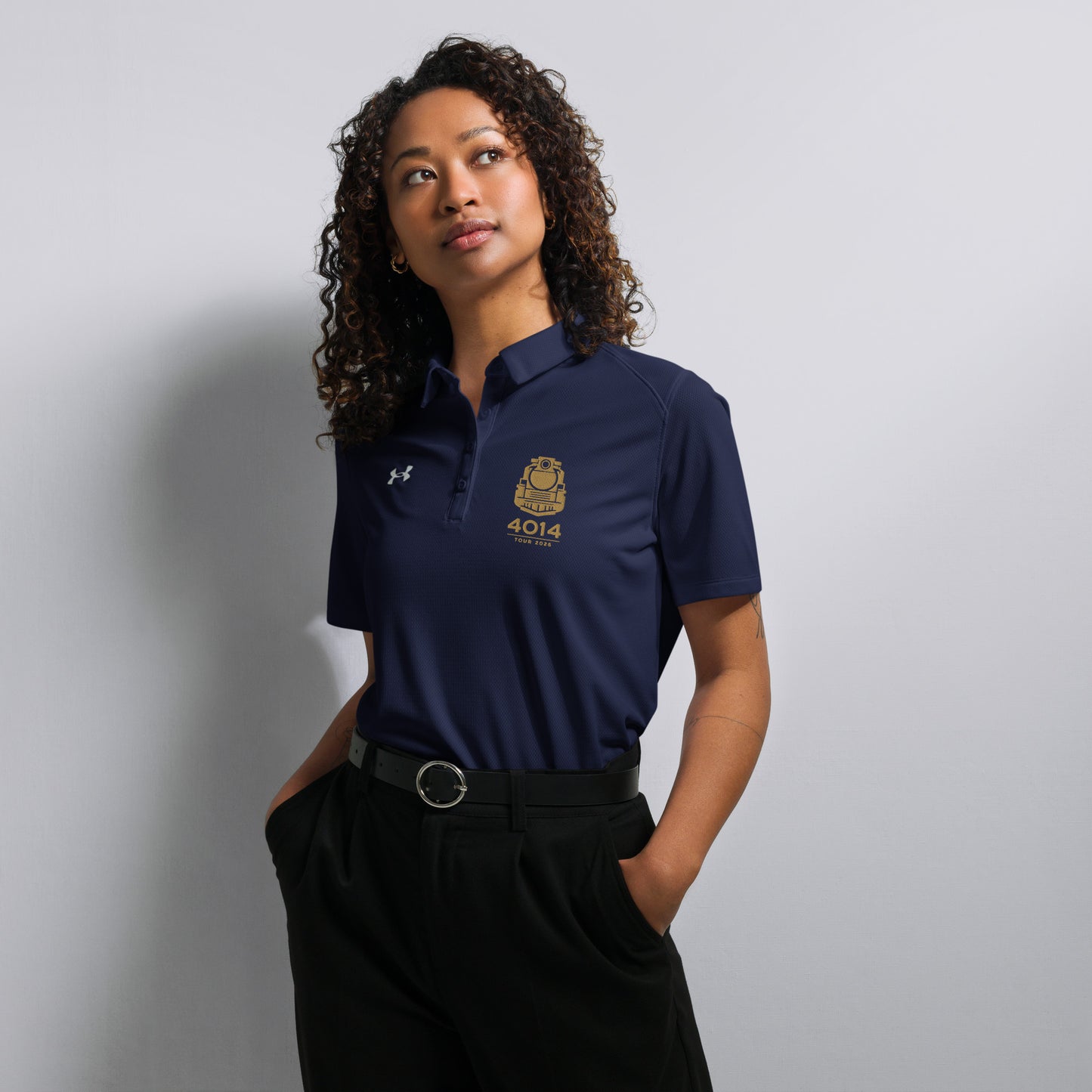 Navy Under Armour women's polo shirt featuring a gold graphic of a front-facing steam locomotive above the text "4014 TOUR 2026" on the left chest. A white Under Armour logo is displayed on the right chest. The shirt has a classic collar and a multi-button placket tailored for a women's fit.