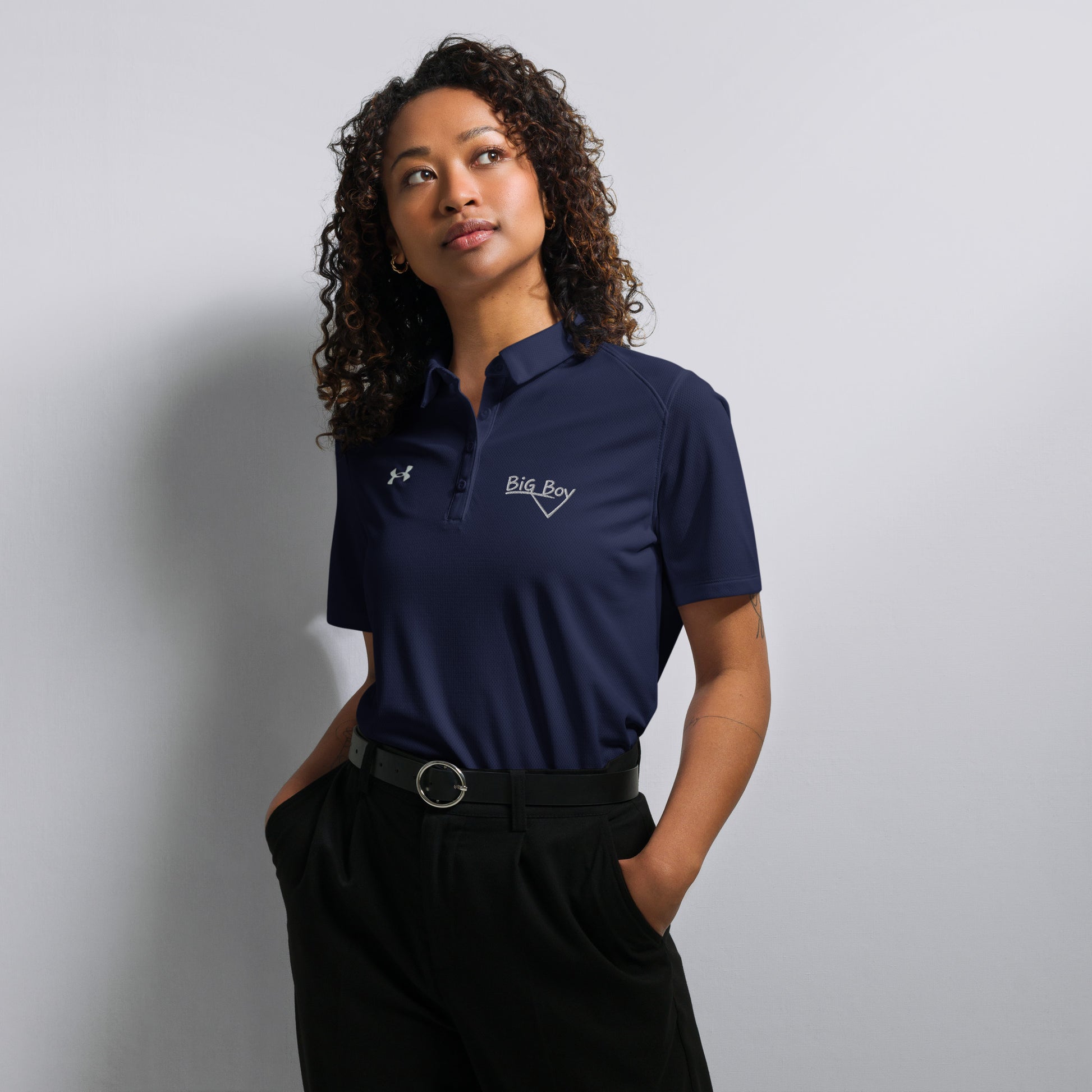 Navy Under Armour women's polo shirt featuring the classic white chalk-style "Big Boy" script logo on the left chest. A white Under Armour logo is displayed on the right chest. The shirt has a classic collar and a multi-button placket tailored for a women's fit.