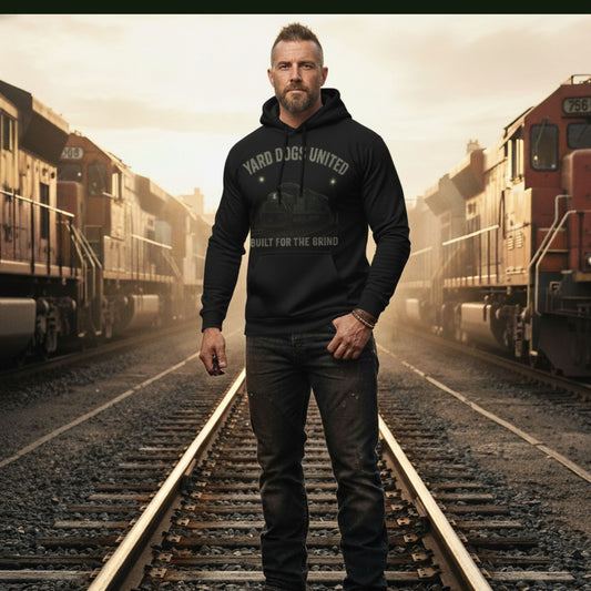 Man wearing a black hoodie with text standing on train tracks with trains in the background