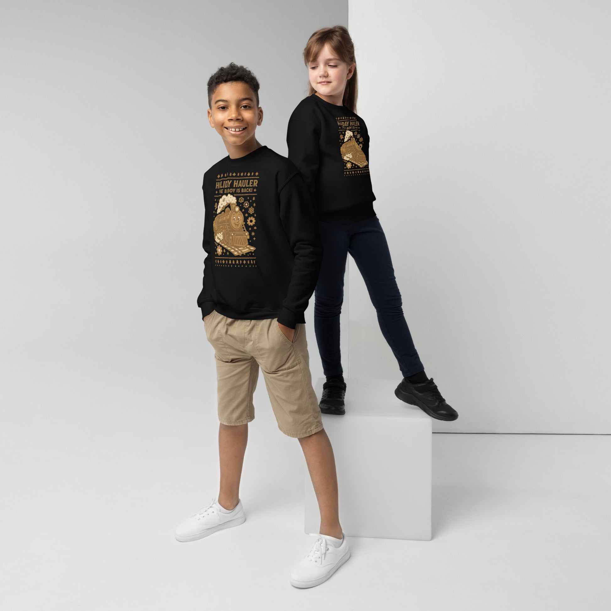 Two children wearing black sweatshirts with gold designs on a white background