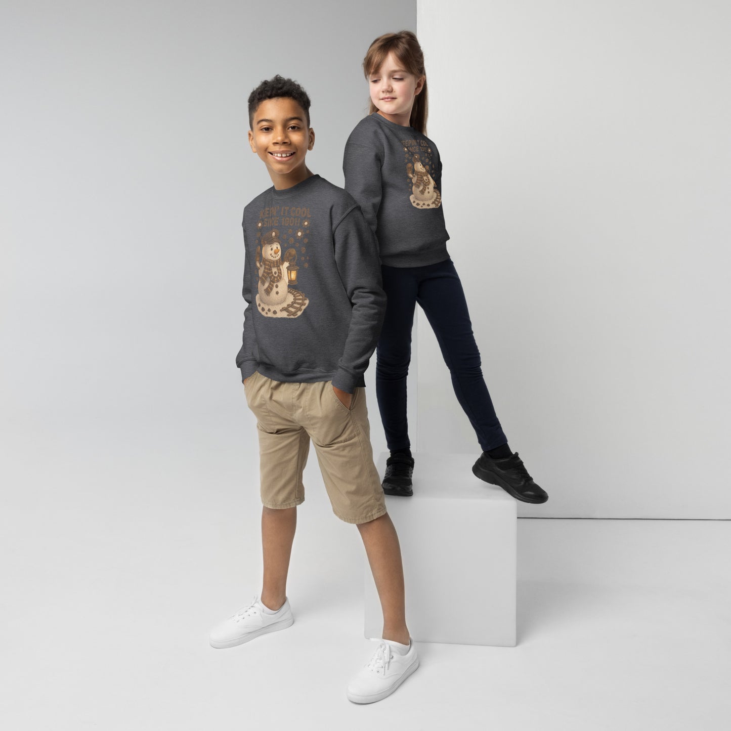 Two children wearing matching dark gray sweatshirts with a snowman design on a white background.